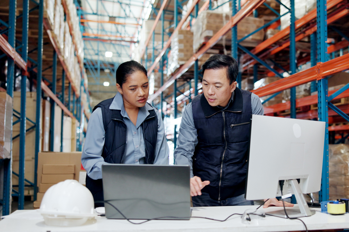 Image of two people talking in front of computer screens inside of a warehouse.
